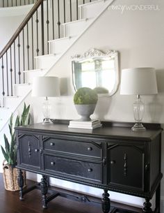 a black dresser sitting under a stair case next to a bannister and mirror