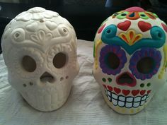 two sugar skulls sitting on top of a white tablecloth covered table next to each other