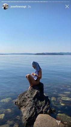 a woman sitting on top of a rock next to the ocean