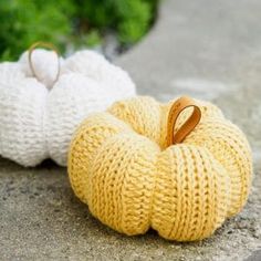 two knitted pumpkins sitting on the ground next to each other, one with a wooden handle