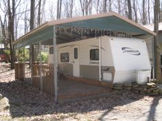 an rv is parked in the woods next to a house with a porch and awning