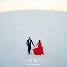 a man and woman holding hands in the middle of a snow covered field at sunset