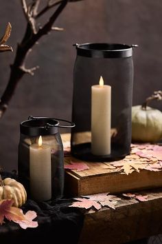 three candles sitting on top of a wooden table next to leaves and pumpkins in the background