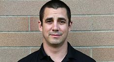 a man standing in front of a brick wall wearing a black dress shirt and tie