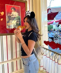 a woman is eating a donut with minnie ears on her head while standing in front of a window