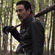 a man with a baseball bat in his hand and wearing a leather jacket, standing in the woods