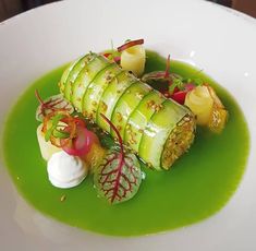 a white plate topped with cucumber covered in green sauce and garnish