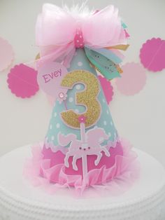 a pink and blue birthday hat on top of a white cake with a number 3