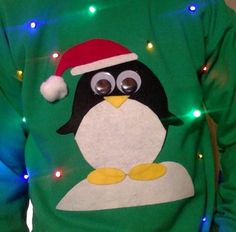 a man wearing a green christmas sweater with a penguin on it's chest and lights around his neck