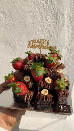 a chocolate cake with strawberries and bananas on top is being held by someone's hand