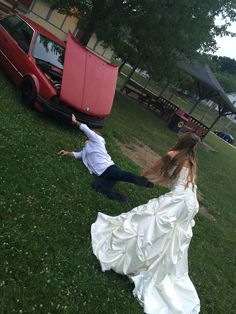 a woman in a wedding dress is falling to the ground next to a red car