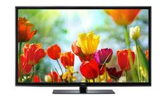 a flat screen tv sitting on top of a wooden table in front of colorful flowers