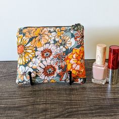 an orange and yellow flowered bag next to two lipstick bottles