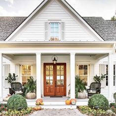 a white house with pumpkins and plants on the front porch, along with two chairs