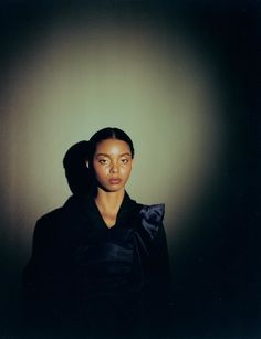 a woman standing in front of a wall with her head turned to the side wearing a black coat