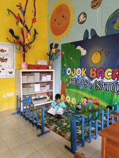 a child is sitting at a table reading a book in front of a colorful wall