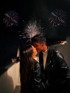 a man and woman kissing with fireworks in the background