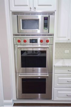 an oven built into the wall in a kitchen with white cabinets and stainless steel appliances