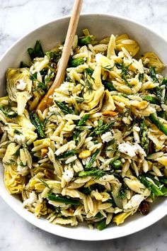 a white bowl filled with pasta and asparagus on top of a marble counter