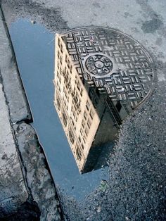 a manhole cover in the middle of a street with a building reflected in it