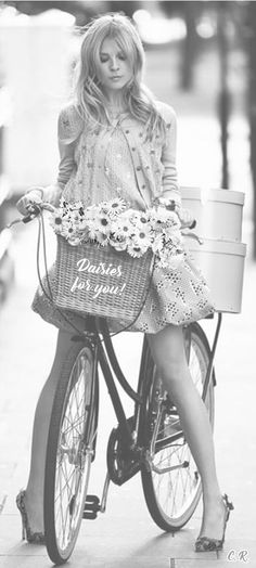 a woman riding a bike with a basket full of flowers