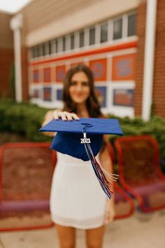 a woman holding a blue graduation cap in front of a building