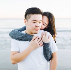 a young man and woman embracing each other on the beach by the ocean at sunset