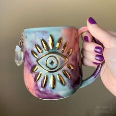 a hand holding a purple and blue coffee mug with an evil eye on the inside