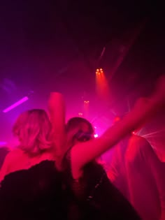 two women are dancing on the dance floor at a party with purple and pink lights