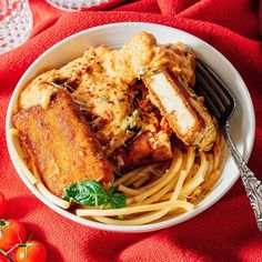 a white bowl filled with pasta and meat on top of a red cloth next to tomatoes