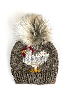 a knitted hat with a white and grey bird on the front, one pom - pom