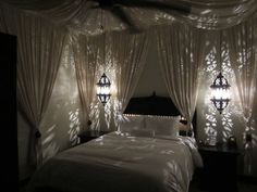 a bed with white sheets and pillows in a room that has curtains on the walls