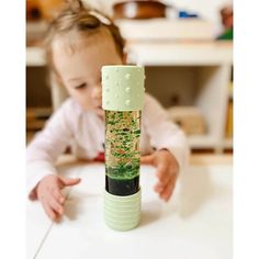 a baby is playing with a green and white object in the middle of a table