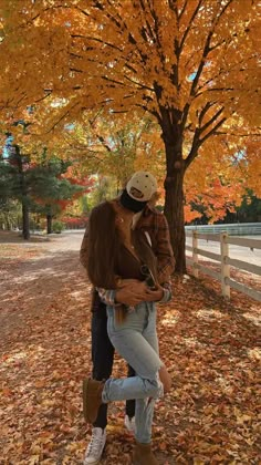 a man and woman standing under a tree in the fall