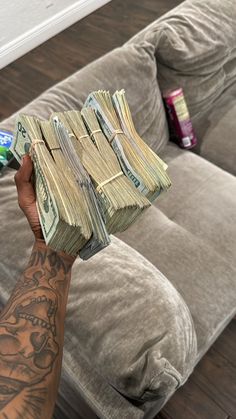 a person holding up stacks of money in front of a couch with tattoos on it