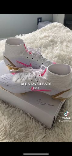 white nike shoes with pink accents on top of a box in the middle of a bed