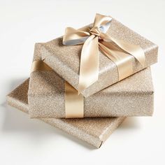 three gift boxes wrapped in shiny gold paper with a bow on top, stacked next to each other