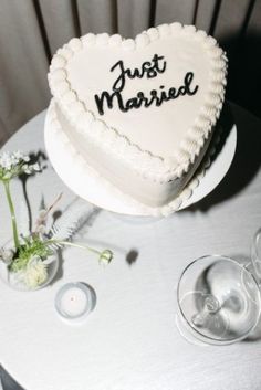 a white heart shaped cake sitting on top of a table next to two wine glasses