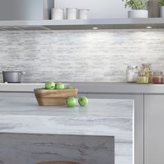 some green apples sitting on a counter in a kitchen with white brick backsplash