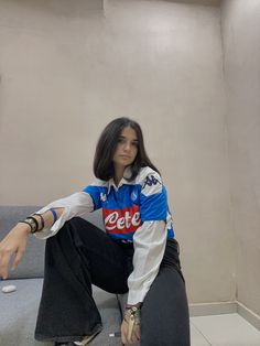 a young woman sitting on top of a couch next to a white wall and holding her hand out