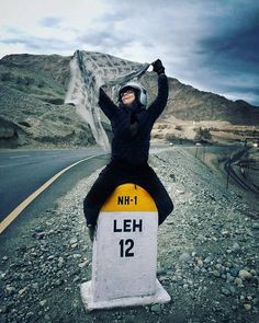 a woman sitting on top of a sign in the middle of the road with her arms up