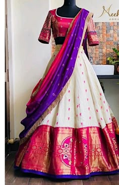 a white and pink lehenga with purple dupatta on the bottom, in front of a mannequin