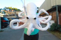 an octopus stuffed animal being held by a woman on the side of the road in front of a building