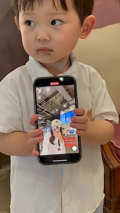 a little boy holding up a cell phone with an image on it's screen