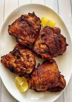 four pieces of chicken on a plate with lemon wedges