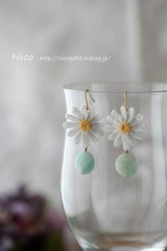 a close up of a pair of earrings with flowers on them in front of a wine glass