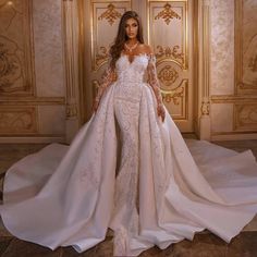 a woman standing in front of a door wearing a wedding dress with long sleeves and high slit