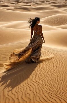 a woman in a long dress walking through the sand dunes with her hair blowing in the wind