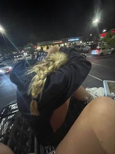 a woman sitting on top of a shopping cart in front of a parking lot at night