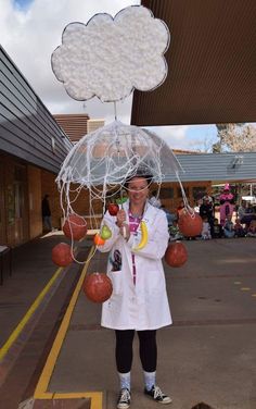 a woman in white coat holding an umbrella over her head with balloons attached to it